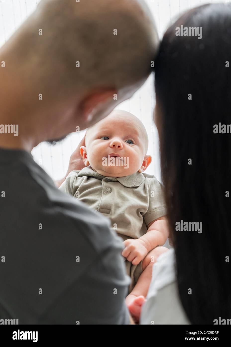 Liebevolle Familie mit neugeborenem Baby. Eltern halten das Kind sanft in den Armen und betrachten es liebevoll. Blick durch die Eltern zum Baby Stockfoto