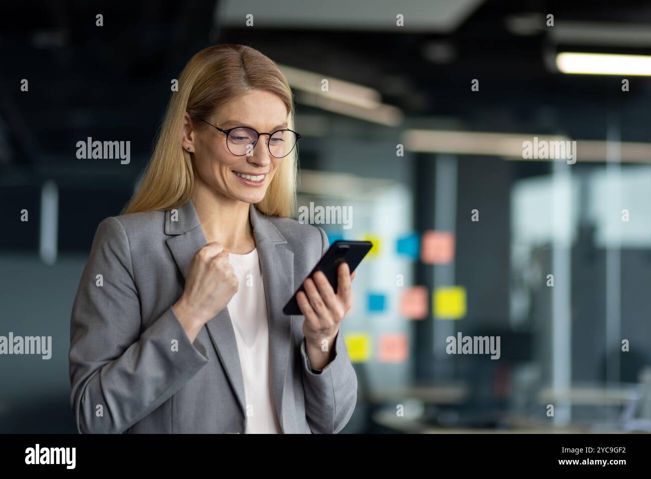 Reife Geschäftsfrau im Büro feiert Erfolg mit Smartphone. Stellt Selbstvertrauen, Führungsstärke und Leistung im beruflichen Umfeld dar. Konz Stockfoto