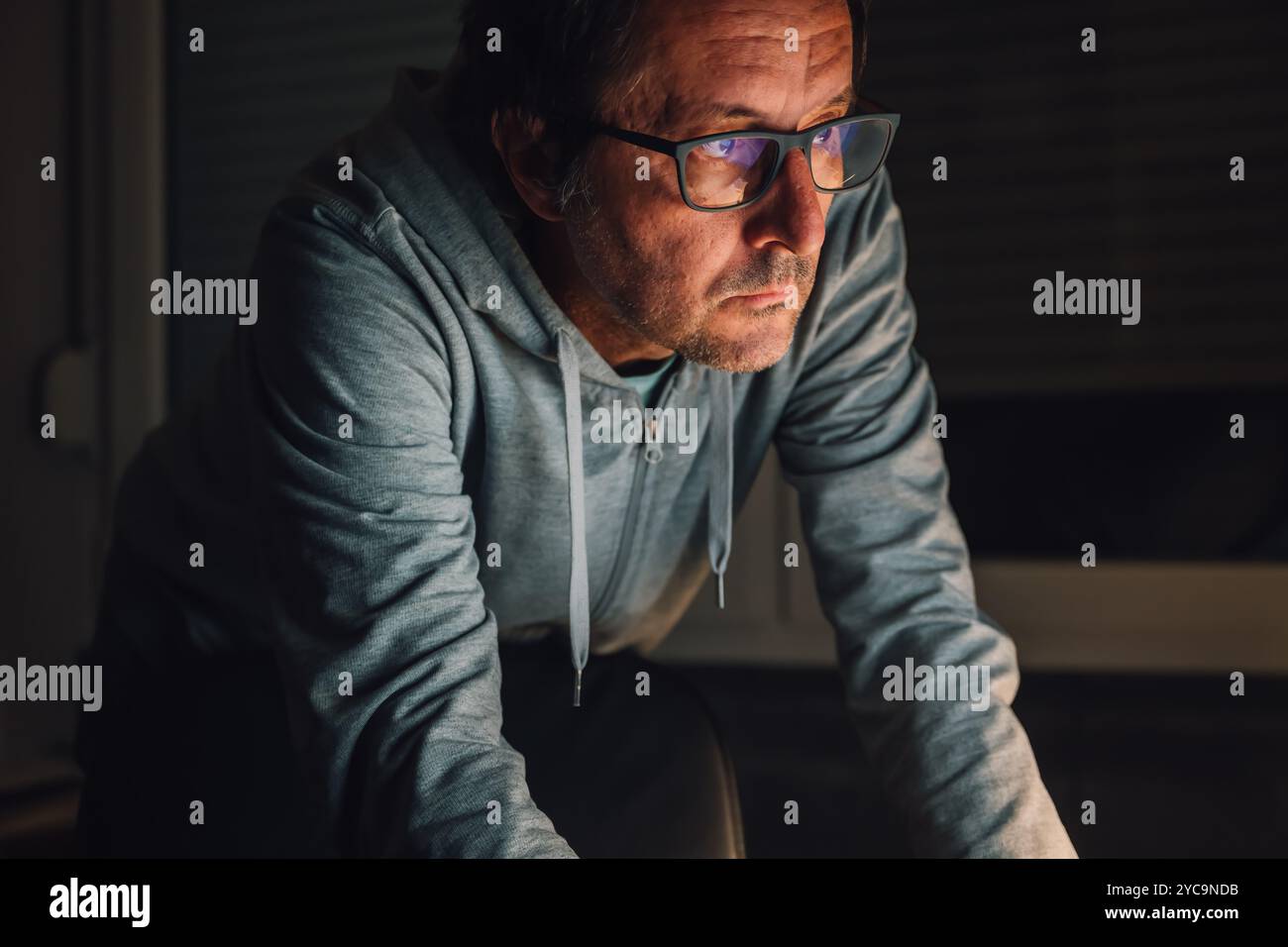 Nahaufnahme Porträt eines männlichen freiberuflichen Arbeiters im dunklen Innenraum des Heimbüros mit Blick auf den Computerbildschirm, selektiver Fokus Stockfoto