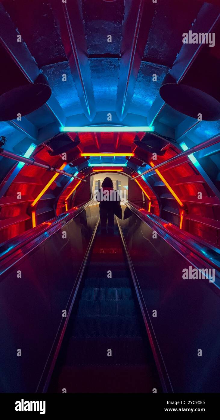 Frau, die eine Rolltreppe hinunterfährt, umgeben von bunten Neonlichtern im Atomium in Brüssel, Belgien. Stockfoto