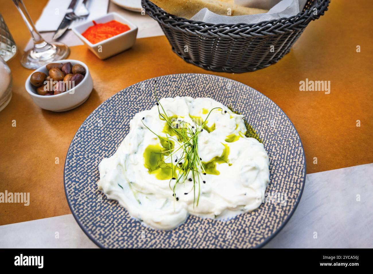 Tzatziki, traditionelle griechische Vorspeise mit Joghurt, Knoblauch, Gurke und Kräuter, Oliven, Brot und Paprika-Dip auf dem Restauranttisch. Stockfoto