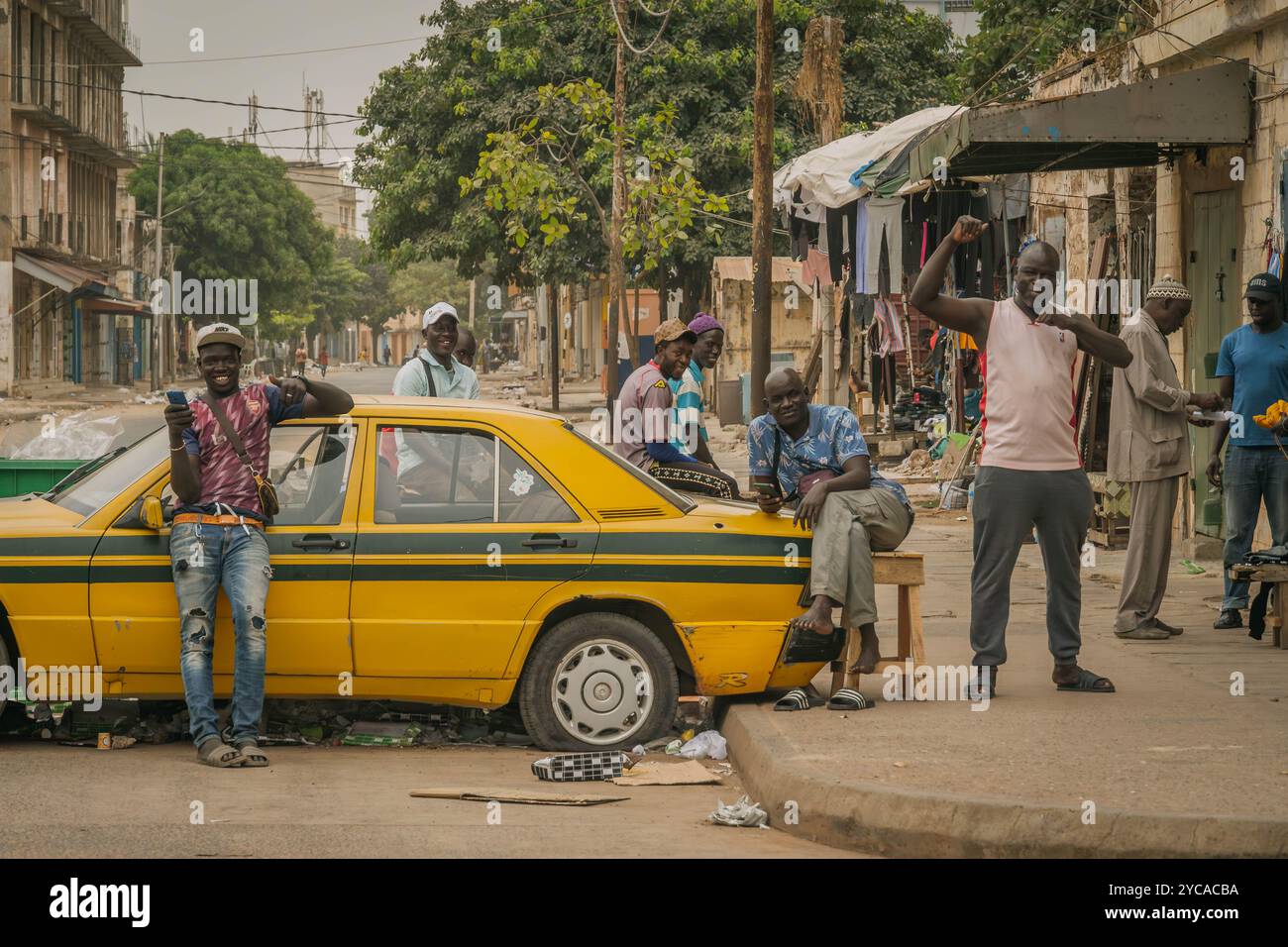 Die Gruppe afrikanischer Männer am gelben Taxiwagen auf den Straßen von Banjul, Gambia. Stockfoto