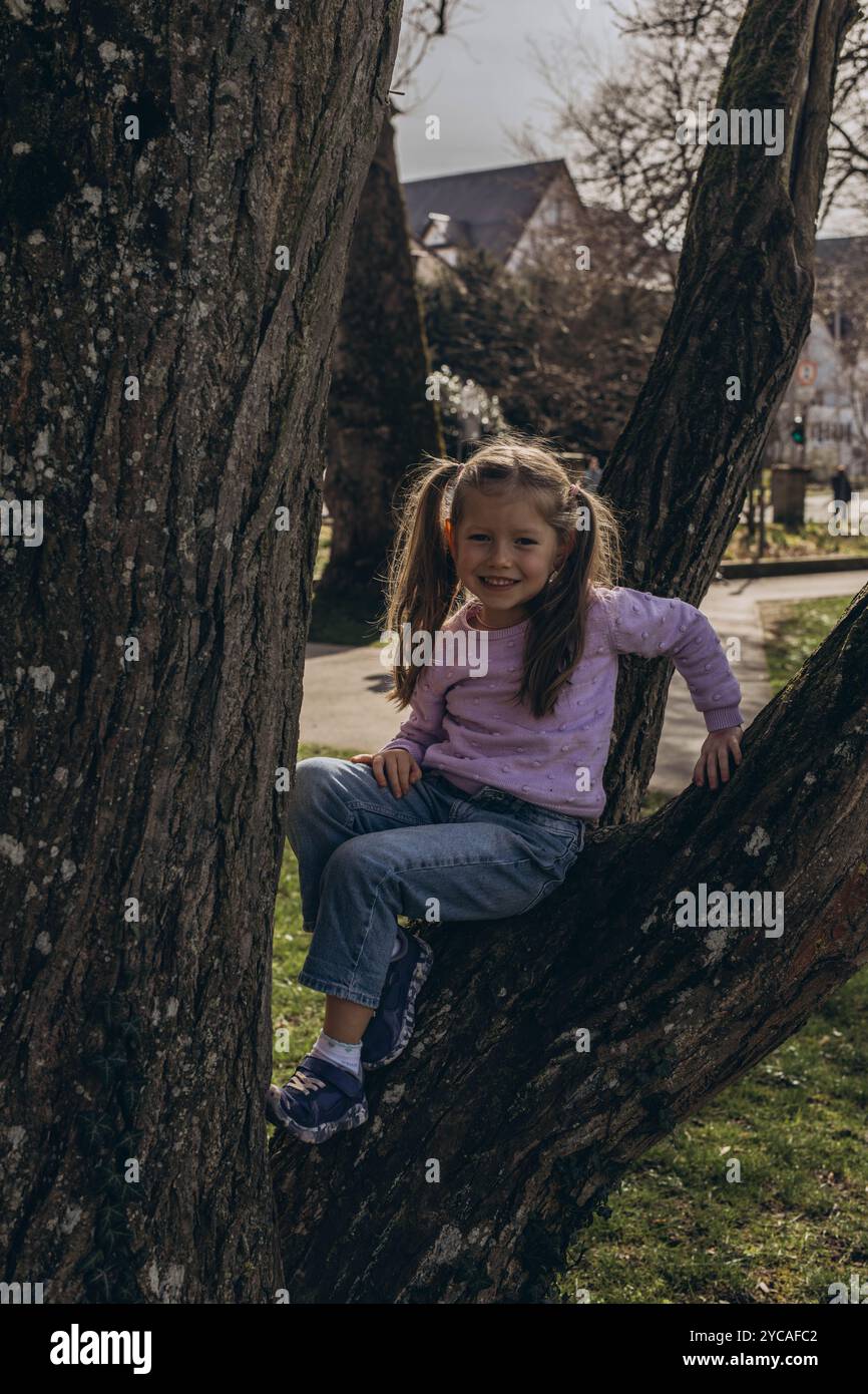 Ein kleines Mädchen ist auf einen Baum geklettert und genießt einen verspielten Moment im Freien. Hochwertige Fotos Stockfoto