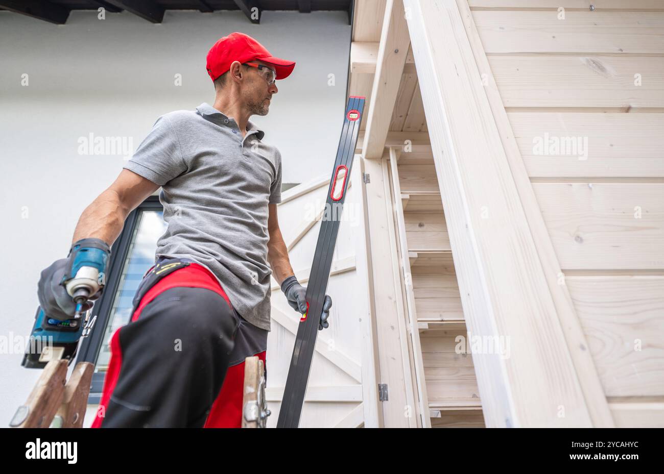 Ein Zimmermann konzentriert sich auf die Nivellierung einer Holzkonstruktion und gewährleistet präzise Messungen bei der Arbeit an einem Bauprojekt in einem Wohnbereich. Stockfoto