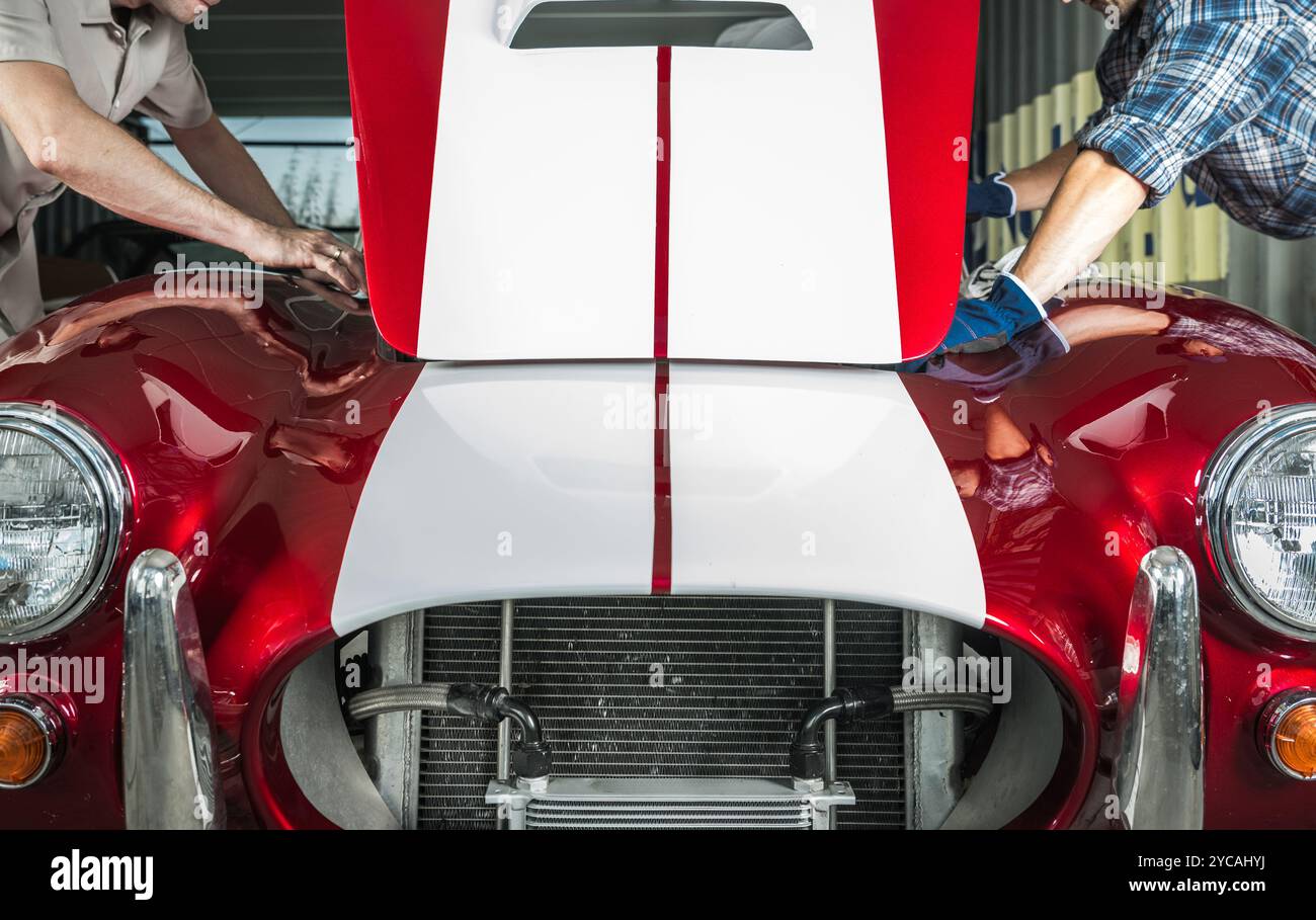 Zwei Personen untersuchen den Motorraum eines roten Oldtimers in einer gut beleuchteten Garage sorgfältig und konzentrieren sich dabei auf Details und Bedingungen. Stockfoto