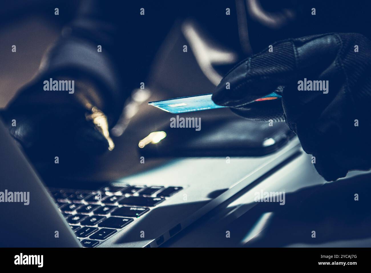 Eine Person mit Handschuhen versucht, Kreditkarteninformationen zu stehlen, während sie an einem Laptop sitzt. Die Umgebung ist dunkel, was auf illegale Aktivi hindeutet Stockfoto