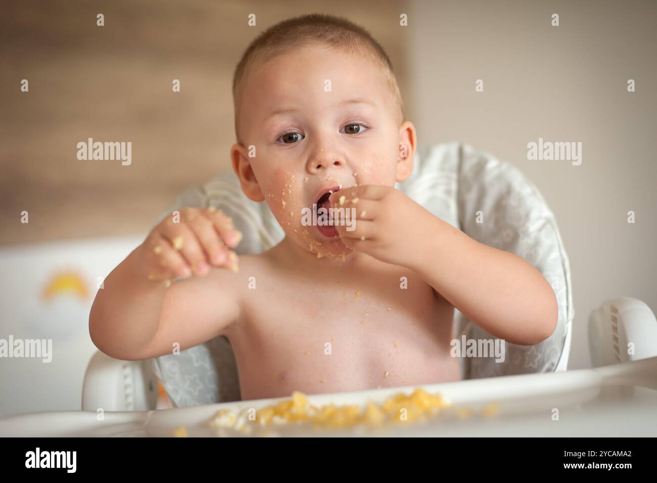 Ein Kleinkind genießt gerne eine Mahlzeit mit seinen Händen, umgeben von einer entspannten Innenumgebung. Das Kind spielt mit dem Essen und zeigt Freude und Kuh Stockfoto