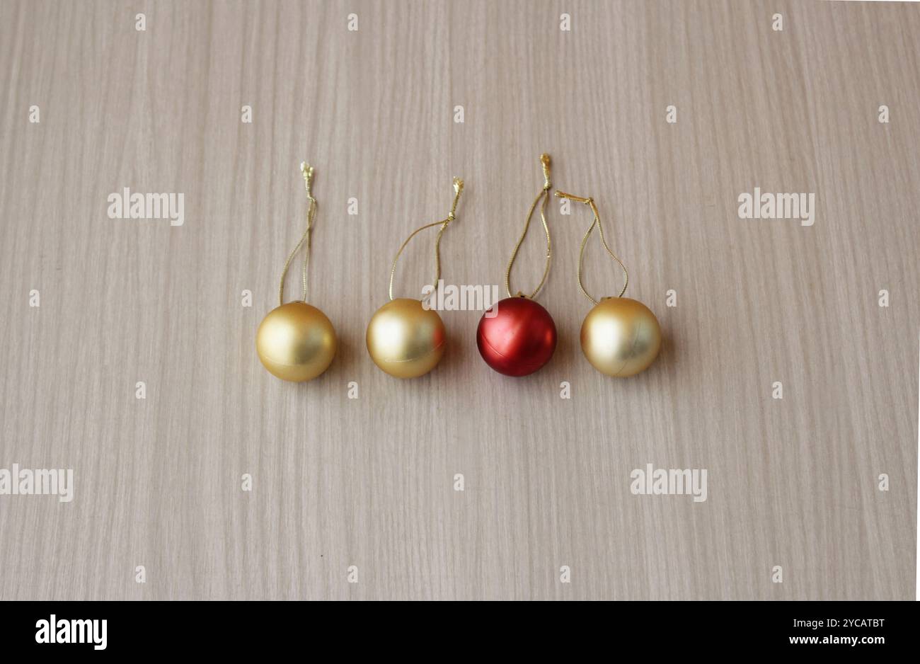 Vier weihnachtskugeln, drei in Goldfarbe und ein Highlight in Rot. Kugeln, Kugeln, Anhänger für Weihnachtsdekoration auf Holzhintergrund. Stockfoto