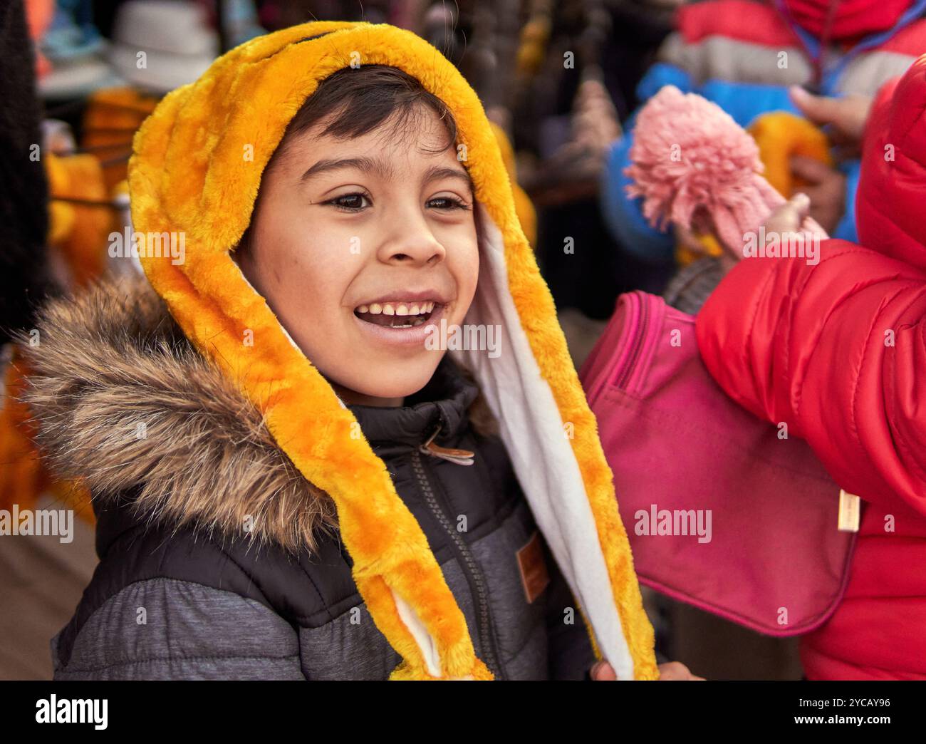 Nahaufnahme eines Latino-Jungen im Profil, der eine Kapuzenjacke mit Pelzbesatz und einen gelben Pelzmütze auf einer Messe in Argentinien trägt. Stockfoto