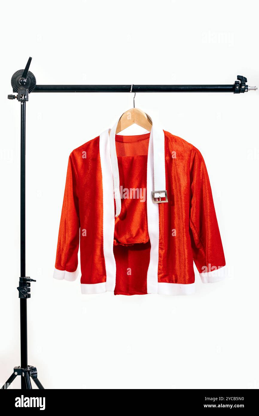 Leuchtend rote Weihnachtsmannjacke mit weißer Besatz, auf einem Holzbügel vor einem strahlend weißen Hintergrund, symbolisiert Feiertagsstimmung und Festlichkeit Stockfoto