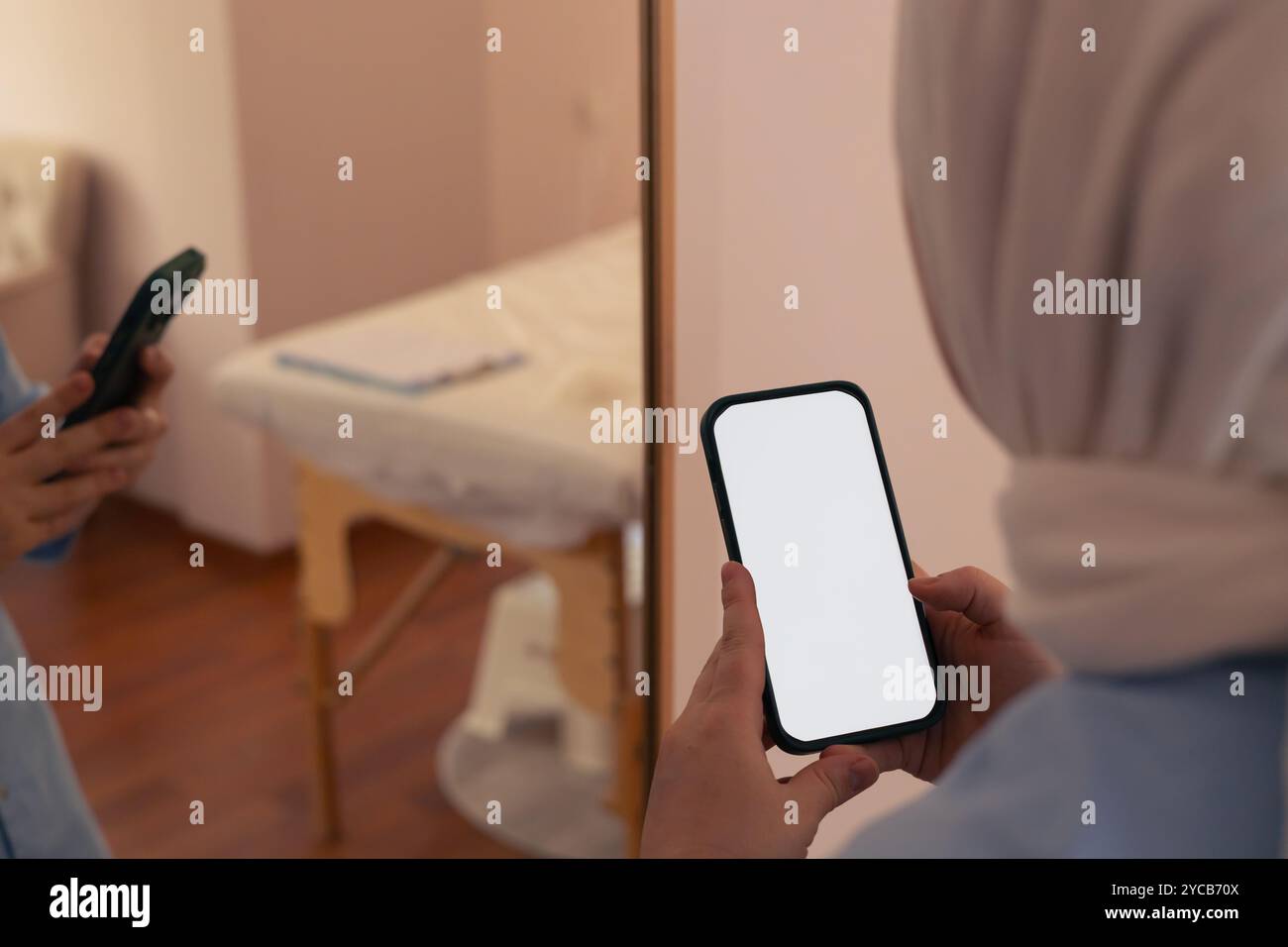 Eine Frau auf der Schürze hält ein leeres Smartphone, während sie in einem sanft beleuchteten Raum steht Stockfoto