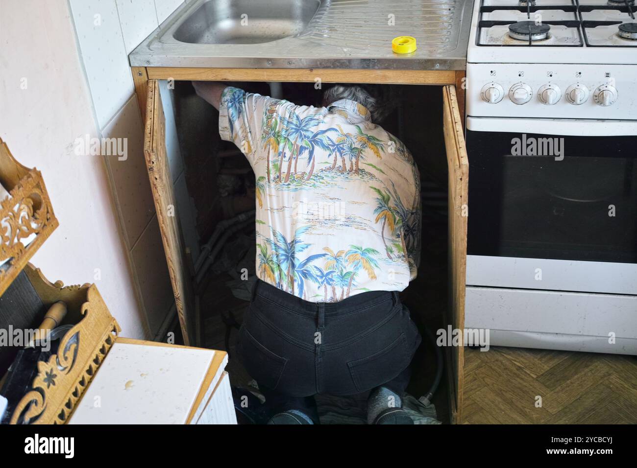Ein Mann auf den Knien, der Wasserarmaturen in einer Küche repariert, Innenaufnahme Stockfoto