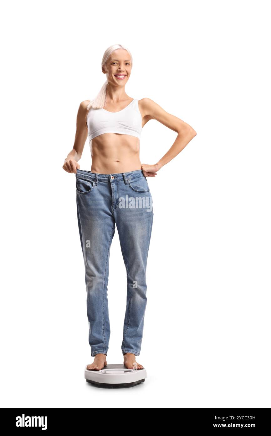 Glückliche junge Frau, die auf einer Waage steht, in einer großen Jeans isoliert auf weißem Hintergrund Stockfoto