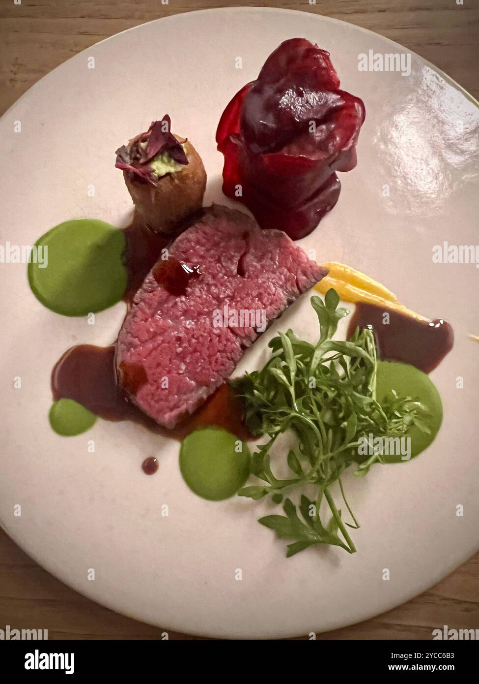 Elegantes Feinschmeckergericht mit mittelseltenem Steak, garniert mit Rucola, Rübenpüree, grüner Kräutersauce und einer kreativen Gemüsekrokette in einer Minute Stockfoto