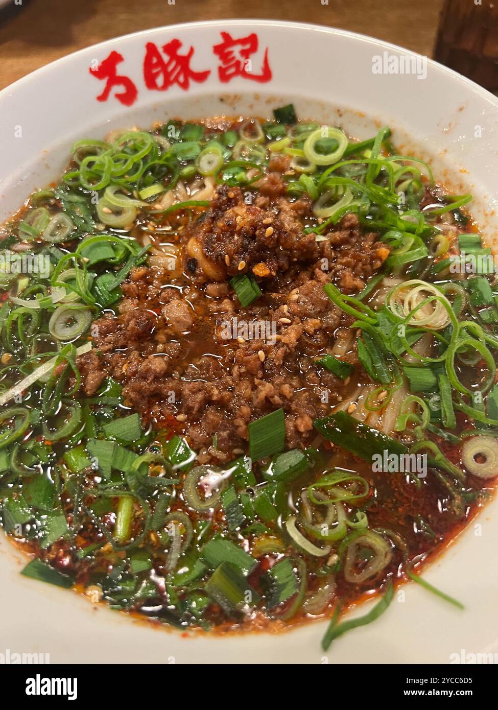Scharfe Dan Dan Dan Dan Nudeln nach Sichuan-Art, garniert mit Schweinehackfleisch, Zwiebeln und einer reichhaltigen Chili-Ölsauce, serviert in einer traditionellen Schüssel Stockfoto