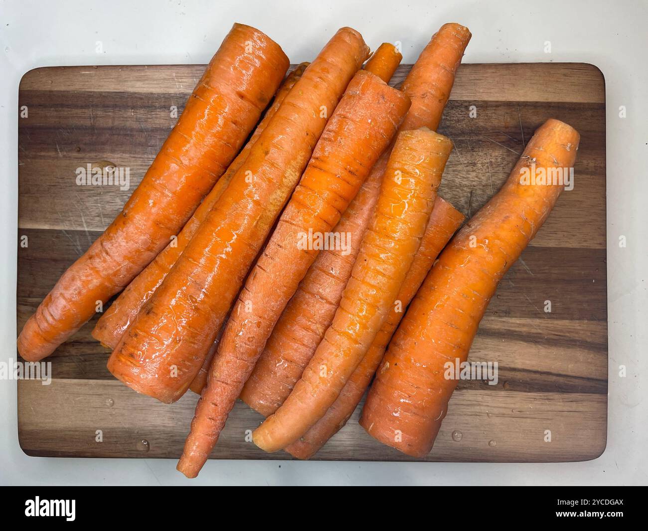 Leuchtende orangefarbene Karotten breiten sich über das hölzerne Schneidebrett aus, ihre Erdtöne und die verschiedenen Formen erzählen Geschichten von frischer Ernte und kulinarischen Versprechen. Stockfoto