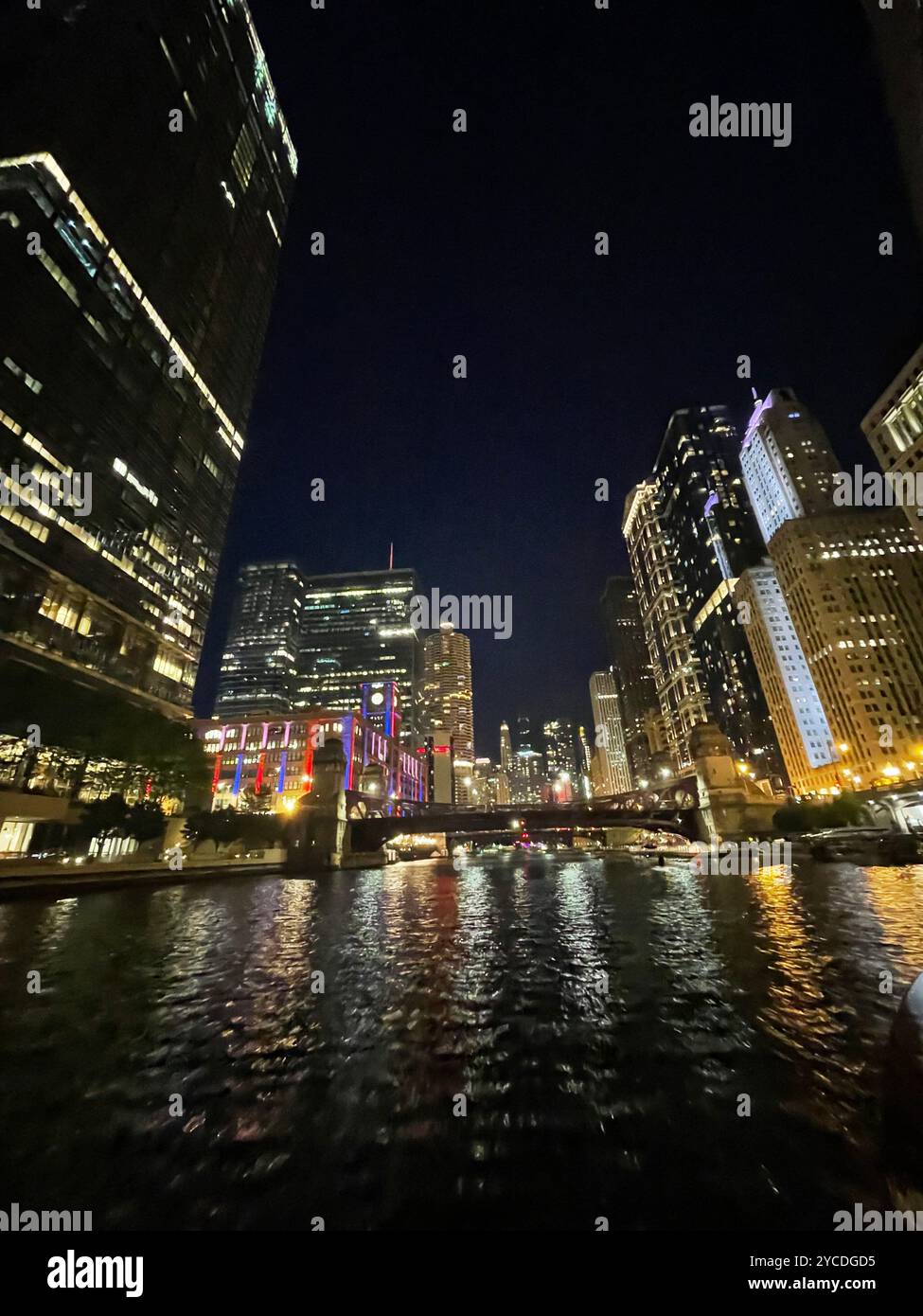 Der Chicago River schlängelt sich durch beleuchtete Wolkenkratzer, deren Lichter auf dunklen Gewässern tanzen, während Brücken die städtischen Canyons in einem nächtlichen Ballett verbinden. - Smartphone-aufgenommenes Stockfoto