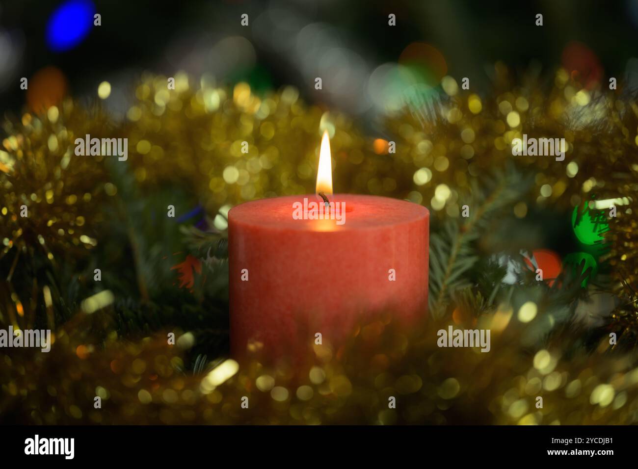 Rote Kerze brennt friedlich, umgeben von Weihnachtskranz und goldenem Lametta in einer ruhigen Umgebung Stockfoto