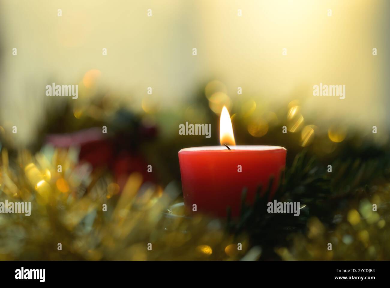 Rote Weihnachtskerze brennt leise in einem Kranz mit goldenem Lametta und weichem Bokeh Stockfoto