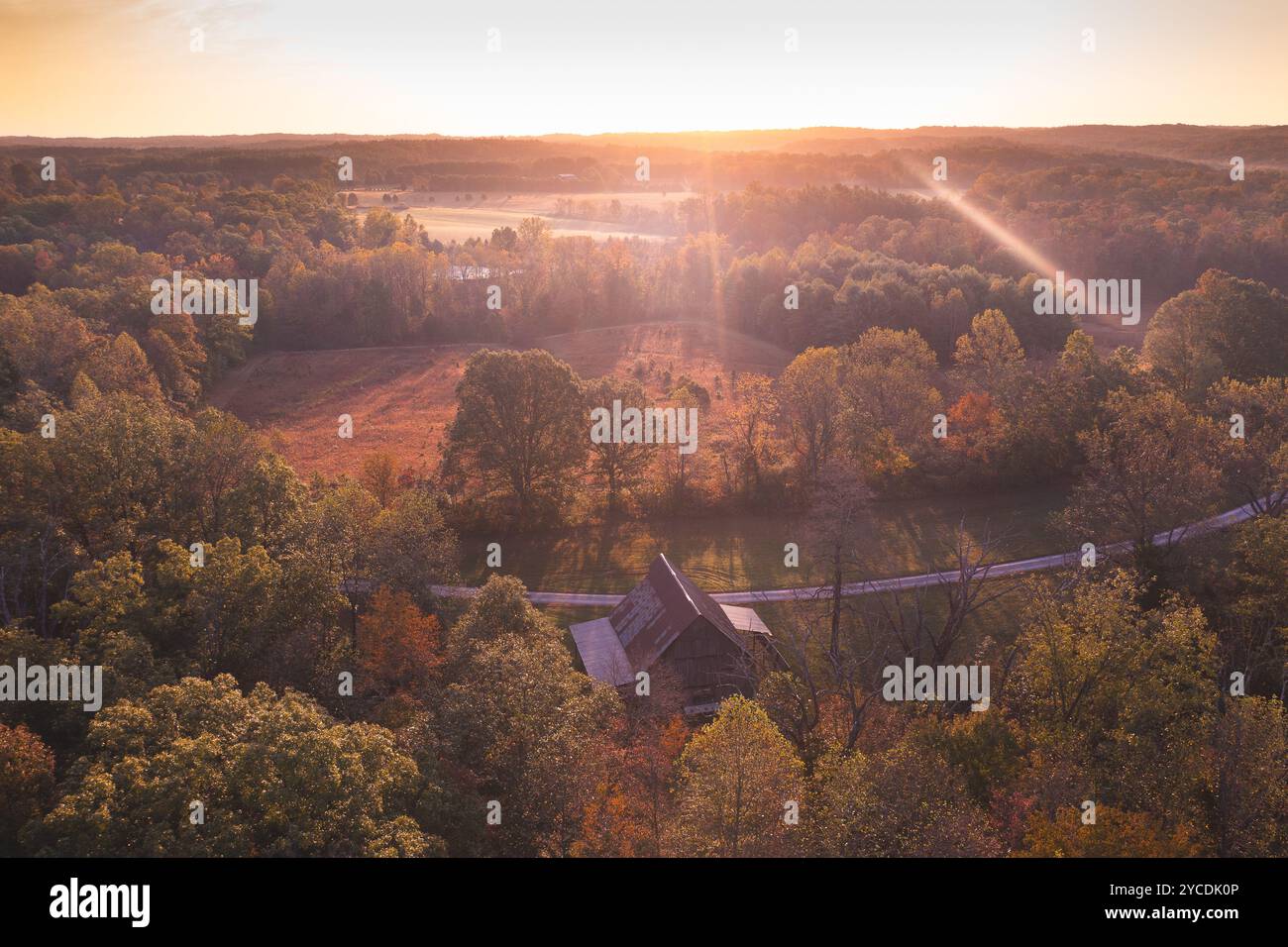 Eine Scheune, die sich inmitten eines Bauernlandes im Süden von indiana befindet. Von hinten mit Blick auf einen hellen Sonnenaufgang. Holz, Lichtungen, Sonnenstrahlen, Linsenfackeln, Antenne Stockfoto