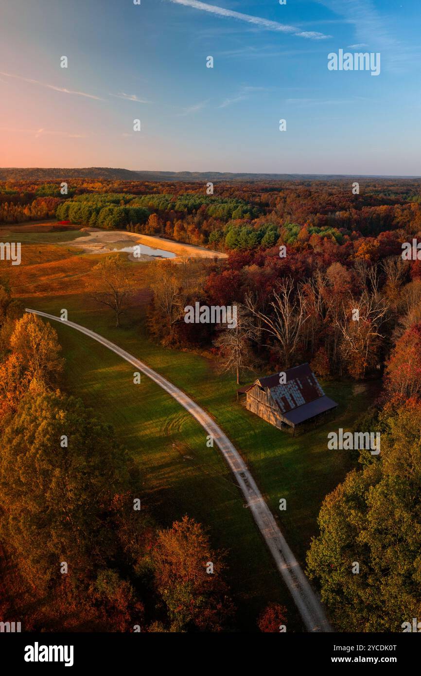 Eine rustikale Scheune befindet sich neben einer Schotterfarm, die durch eine Waldlichtung führt. Der Hoosier National Forest umgibt die dünnen Wolken darüber Stockfoto
