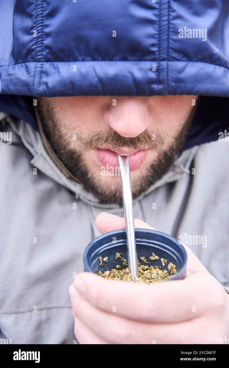 Porträt eines jungen argentinischen Mannes, ein traditionelles Heißgetränk, an einem kalten Wintermorgen. Nahaufnahme der Komposition, die Kapuze der Jacke Stockfoto