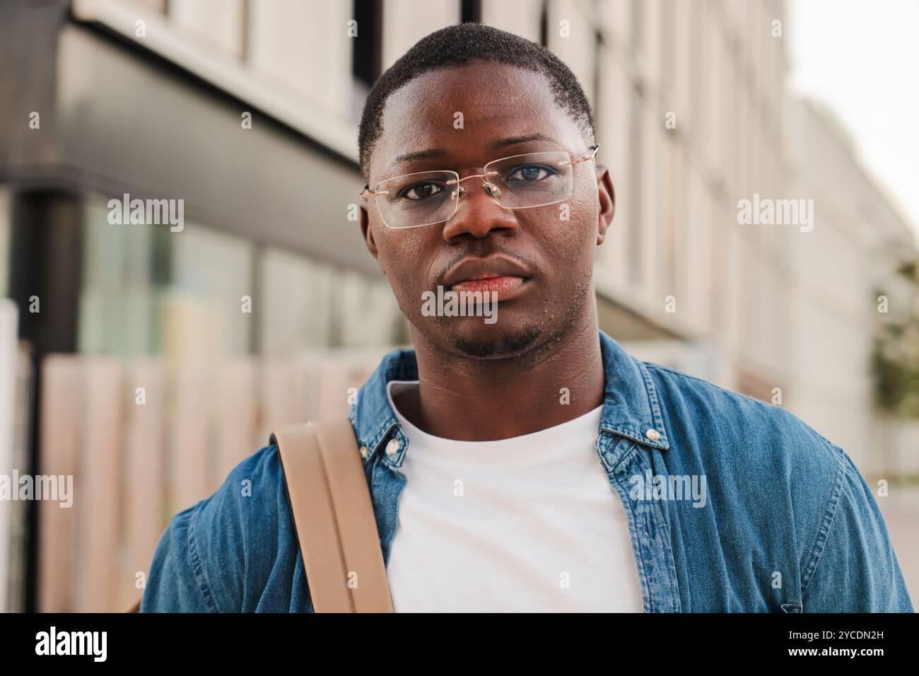 Ernsthafter after afroamerikanischer Student, der nachdenklich in die Kamera blickt, eine Mappe hält und einen Rucksack trägt, im Freien in einer modernen urbanen Umgebung steht und Selbstvertrauen auf dem Universitätscampus ausdrückt. Hochwertige Fotos Stockfoto