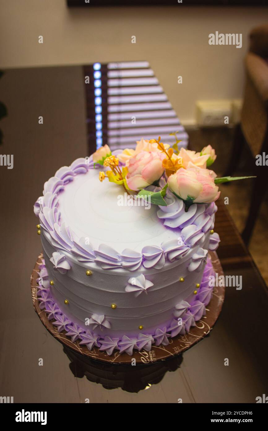 Sonnenlicht strömt durch das Fenster und beleuchtet den Kuchen mit seinem pastellfarbenen violetten Zuckerguss und bezaubernden Blumendekorationen wunderschön Stockfoto