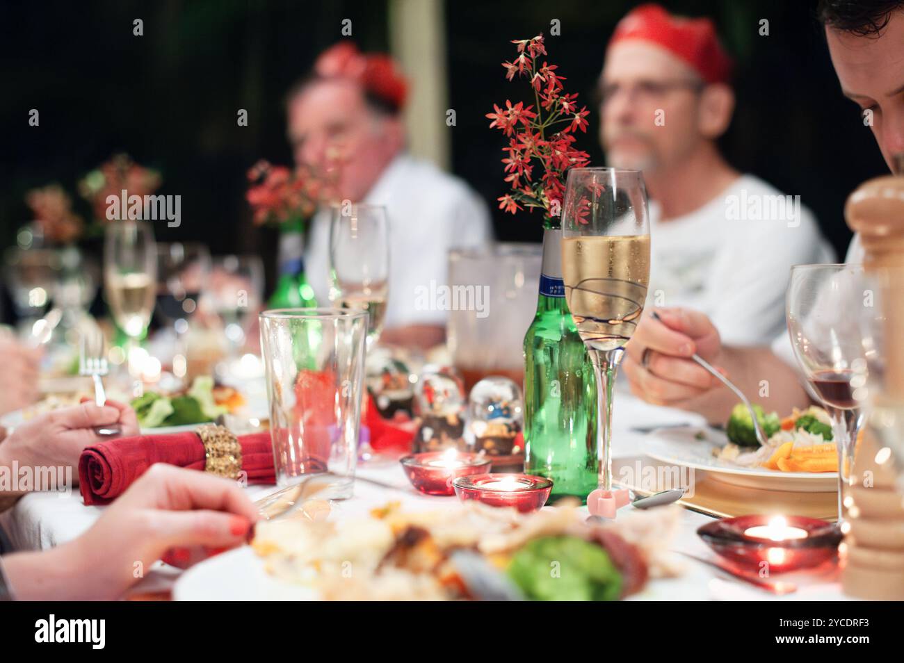 Eine Familie sitzt an dem in Rot und Grün und Gold dekorierten Esstisch und teilt ein Festmahl Stockfoto