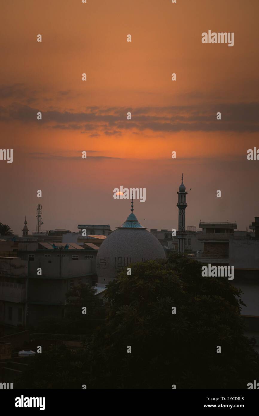 Goldene Farbtöne prägen den Abendhimmel, während Vögel über die Moschee gleiten und die Kuppel und das Minarett in einer ruhigen Silhouette bei Sonnenuntergang einrahmen. #EveningGlow #Cityscape Stockfoto