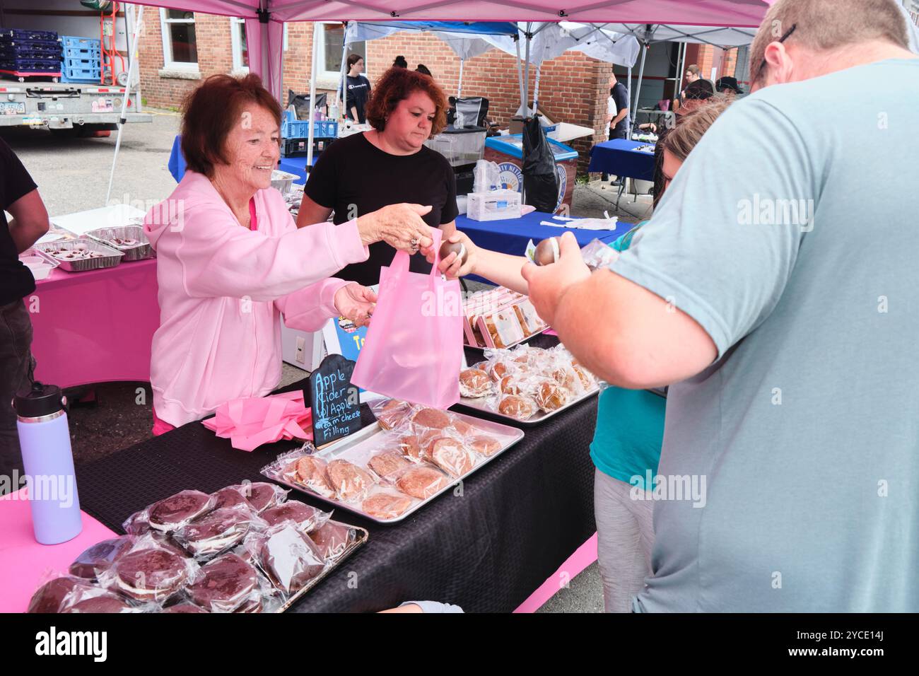 Eine Frau in Rosa, die an einem Stand Kuchen verkauft. Beim Whoopie Pie Festival in Dover-Foxcroft, Maine, New England, USA Stockfoto