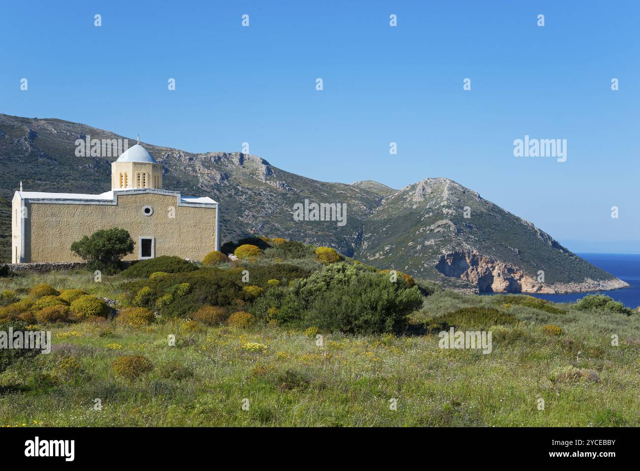 Kleine Kirche vor einer Bergkulisse am Meer mit einem klaren blauen Himmel, umgeben von grüner Landschaft, Chiesa di Agia Triada, Kirche in der Nähe von Marmari, Stockfoto