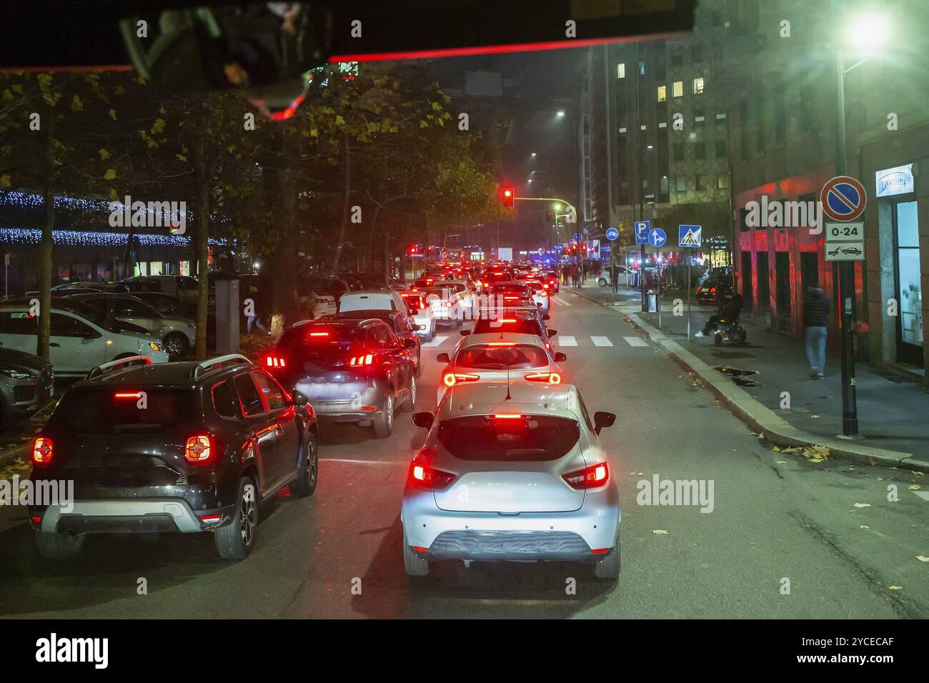 12-10-2022 Mailand, Italien. Verkehr in Mailand, Nacht. Behinderte Person für einen Spaziergang in einem elektrischen Rollstuhl an der Kreuzung. Verschwommene Bewegungen Stockfoto