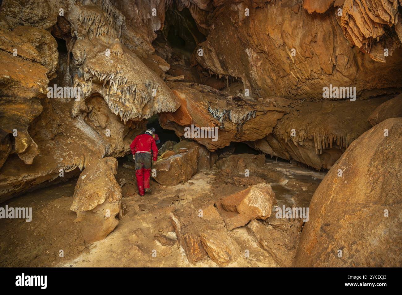 Ein Speläologe mit Helm und Scheinwerfer, der eine Höhle mit reichen Stalaktiten- und Stalagmitenformationen erforscht. Grafik Stockfoto