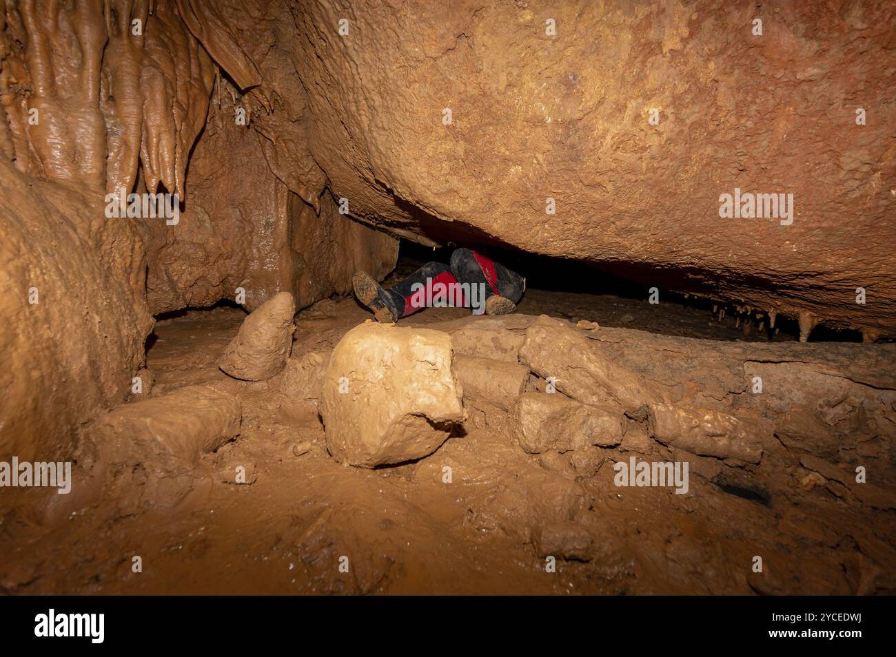 Ein Speläologe mit Helm und Scheinwerfer, der eine Höhle mit reichen Stalaktiten- und Stalagmitenformationen erforscht. Grafik Stockfoto