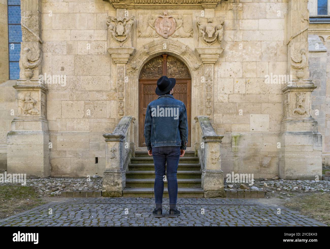 Ein junger Touristenmann, der vor einer schönen mittelalterlichen Chatedral-Tür steht. Ein Mann vor einer Eingangstür einer alten Architekturkirche in Alba IUL Stockfoto