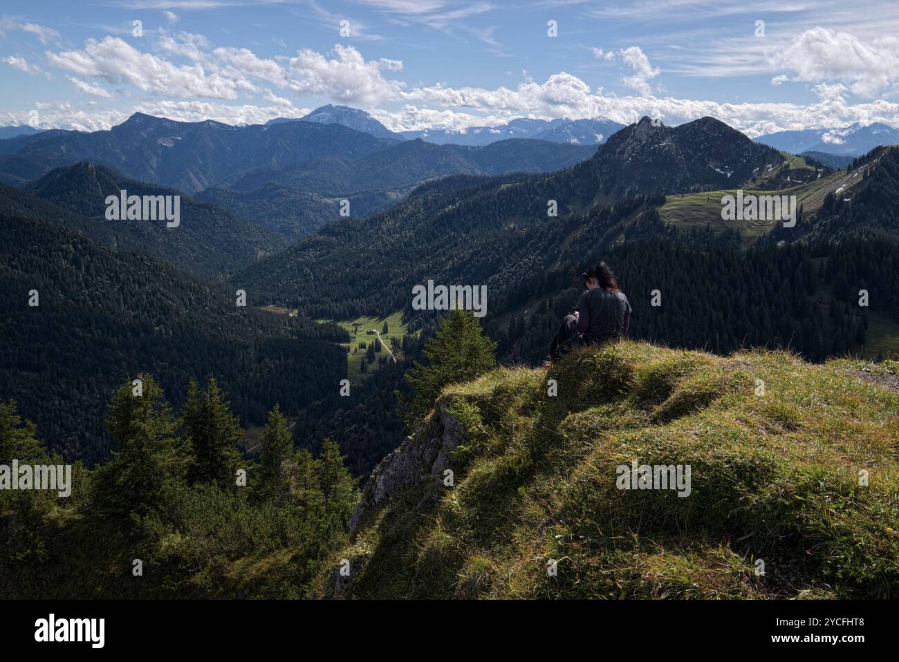 Frau, die am Rande eines Berggipfels vor dem Bergpanorama sitzt Stockfoto