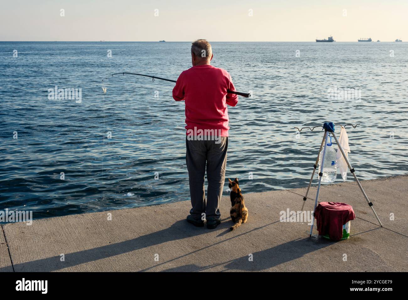 Ein Mann, der im Bosporus fischt, während seine Katze auf Titten wartet, Istanbul, Türkei Stockfoto