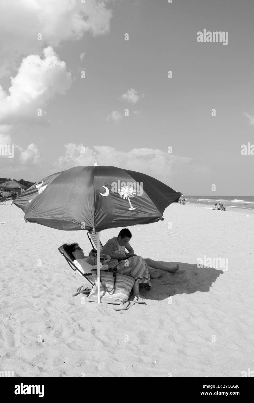 Kaukasisches Paar sitzt unter einem Sonnenschirm am Grand Strand in Myrtle Beach, South Carolina, USA. Stockfoto