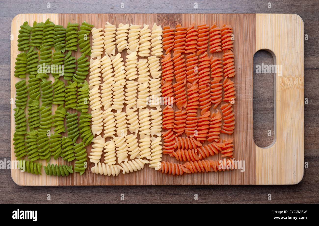 Spiralen, Spirelli oder Fussili Tricolore Nudeln in den italienischen Nationalfarben, grün, weiß, rot auf einem Bambus Küchenbrett Stockfoto