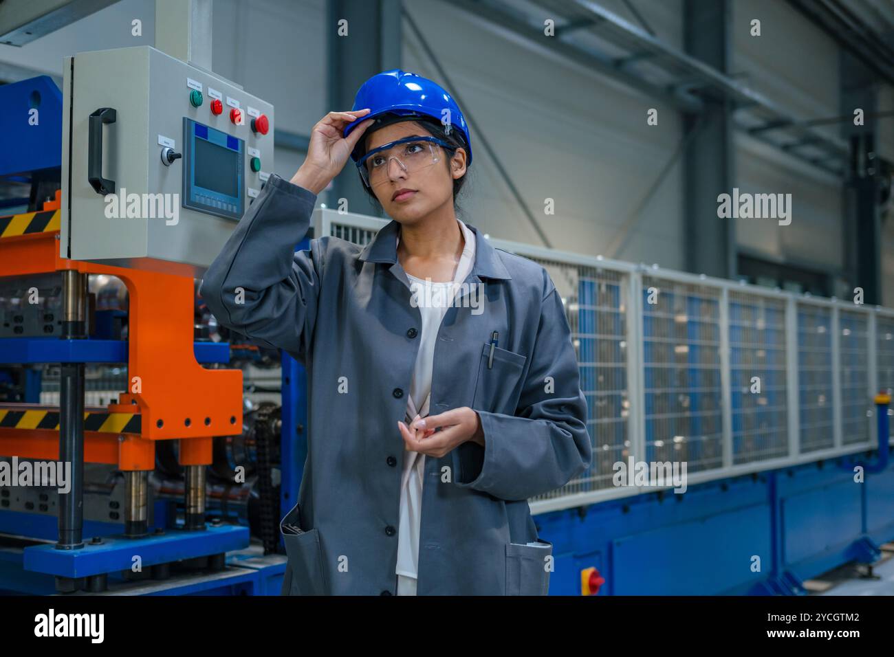 Weibliche Fabrikingenieurin überwacht die Schalttafeln und bedient den automatisierten Fertigungsprozess. Stockfoto