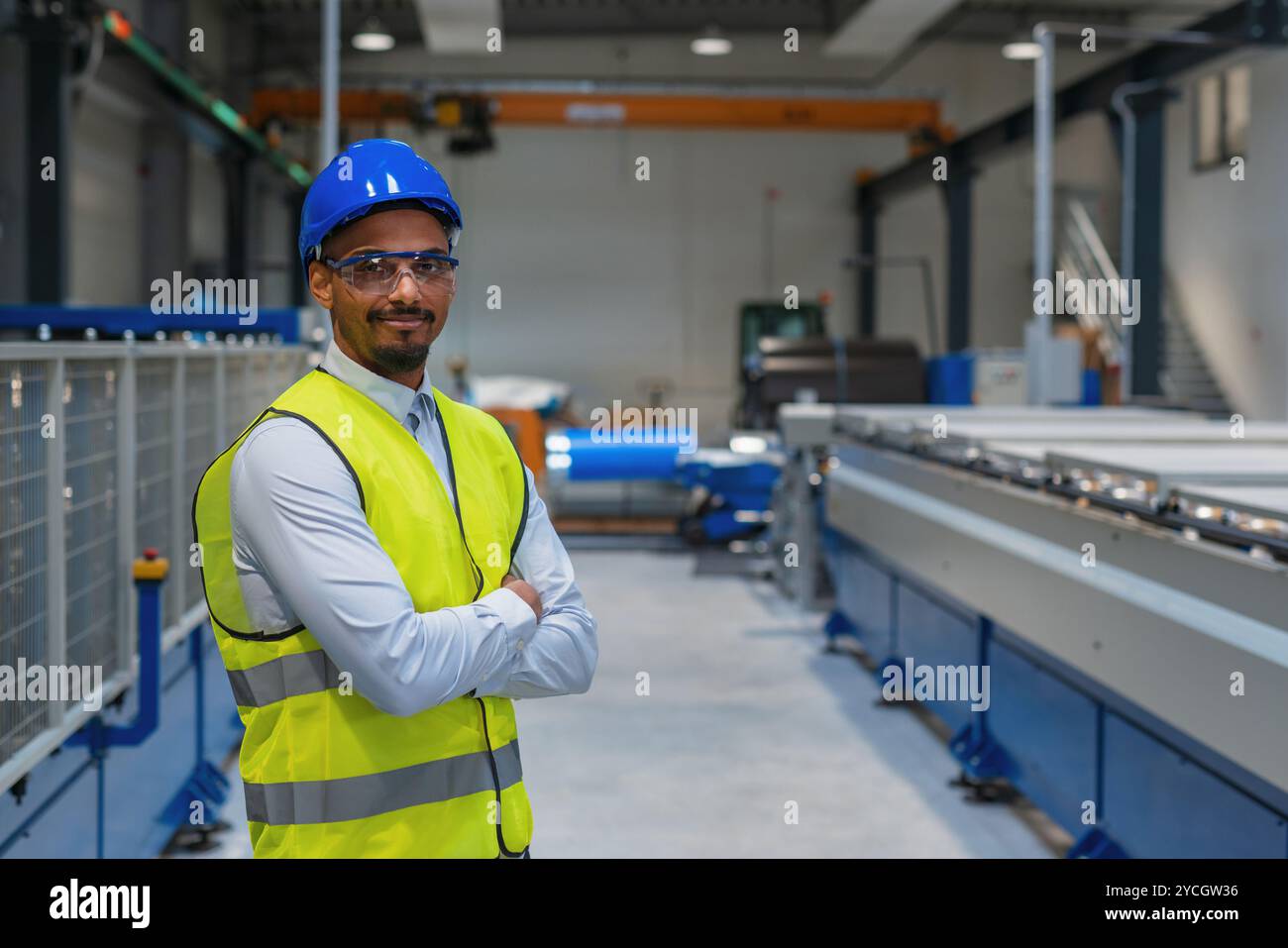 Fertigungsingenieur in einer Fabrik mit gelber Weste und blauem Helm bei der Arbeit. Stockfoto