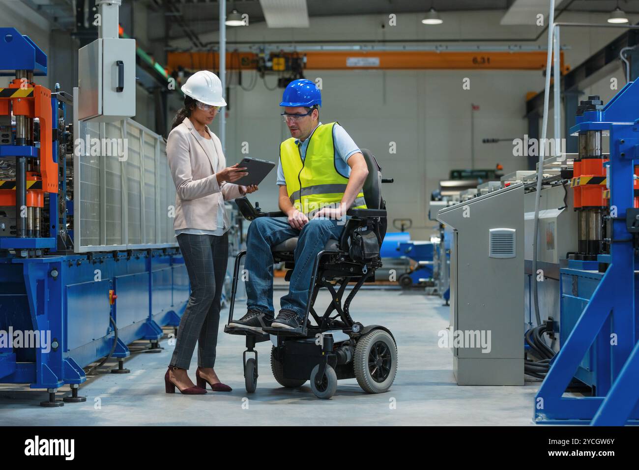 Weibliche Führungskraft, die einen neuen Mitarbeiter mit einer Behinderung für einen Job ausbildet, erklärt die Arbeit an Maschinen. Industrie, Integration und Arbeitsplatzkonzept. Stockfoto