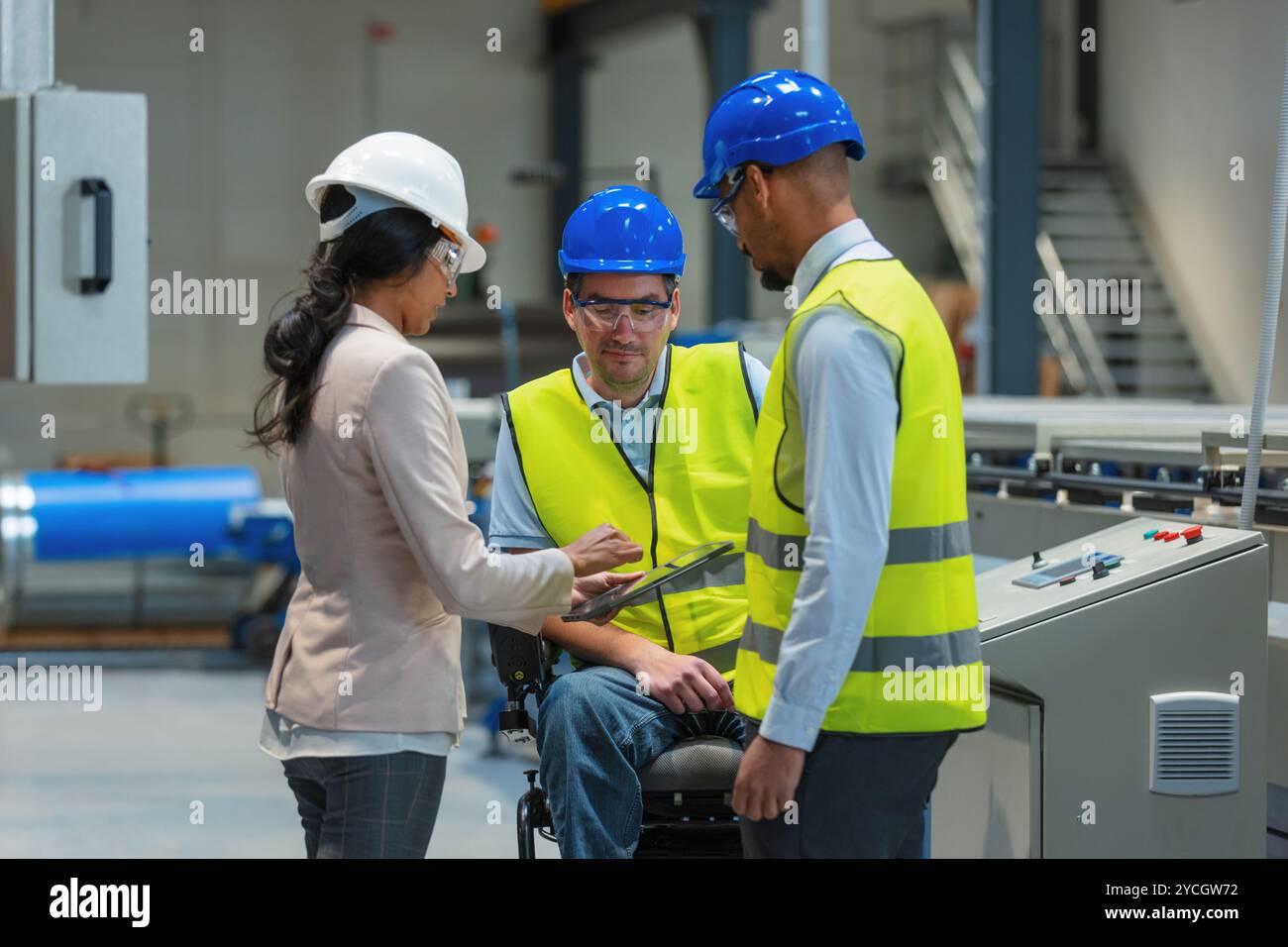 Weibliche Führungskraft spricht mit zwei Arbeitern an der Produktionslinie, darunter einer mit Behinderung, über den Produktionsprozess. Stockfoto