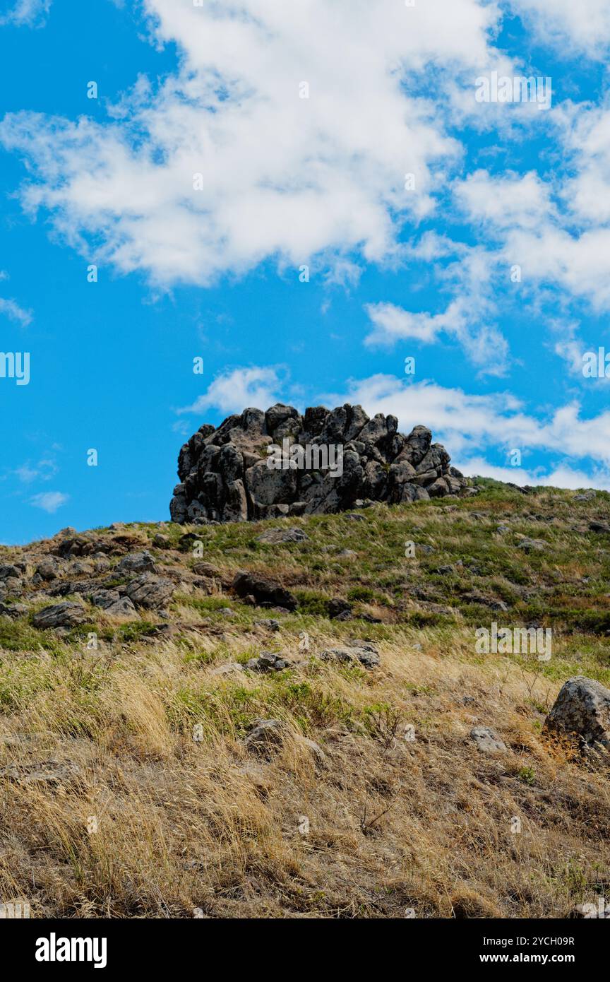 Eine zerklüftete Felsformation befindet sich auf einem grasbewachsenen Hügel unter dem blauen Himmel bei Vereda da Ponta de São Lourenco Stockfoto