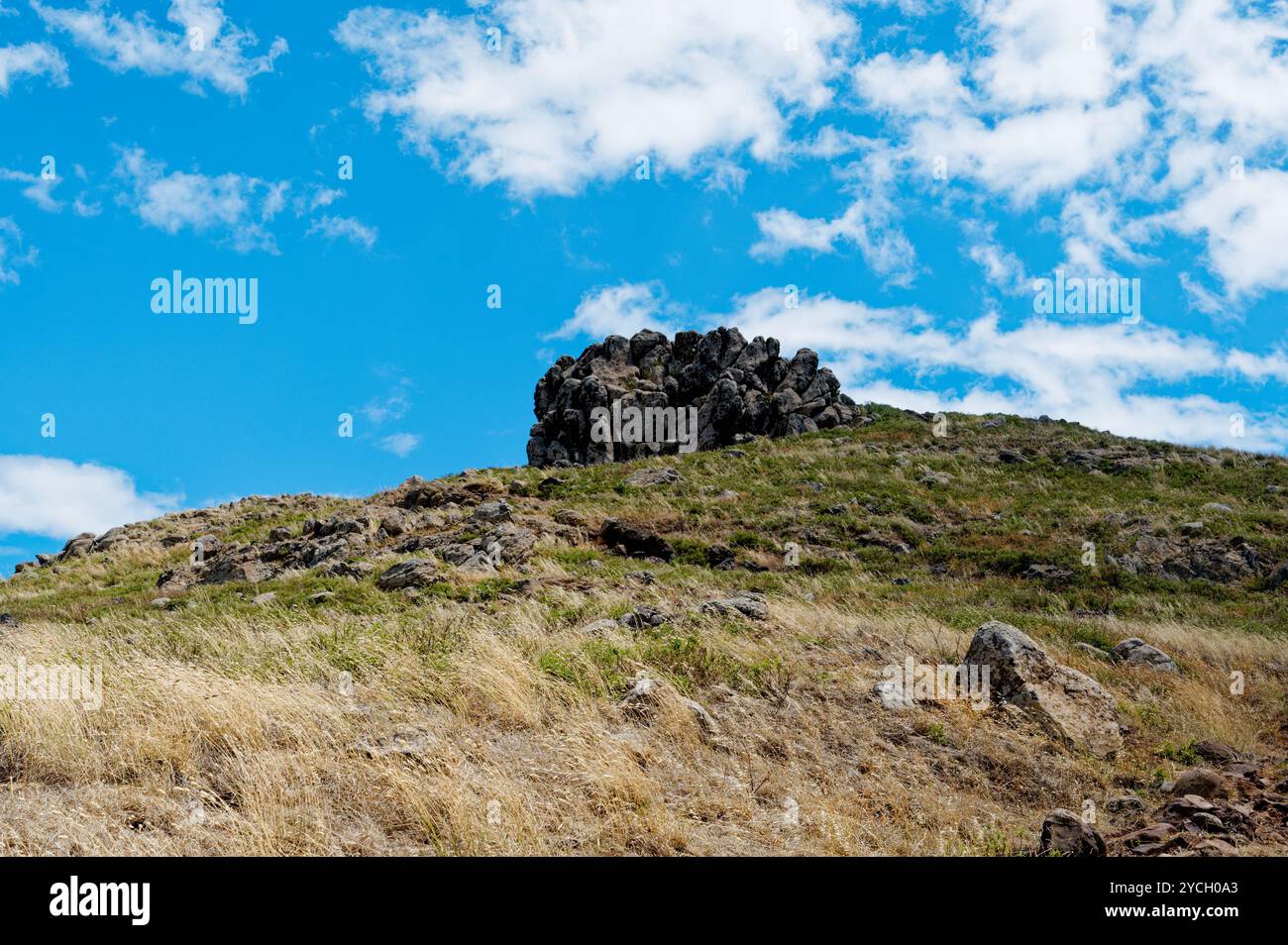 Eine zerklüftete Felsformation befindet sich auf einem grasbewachsenen Hügel unter dem blauen Himmel bei Vereda da Ponta de São Lourenco Stockfoto