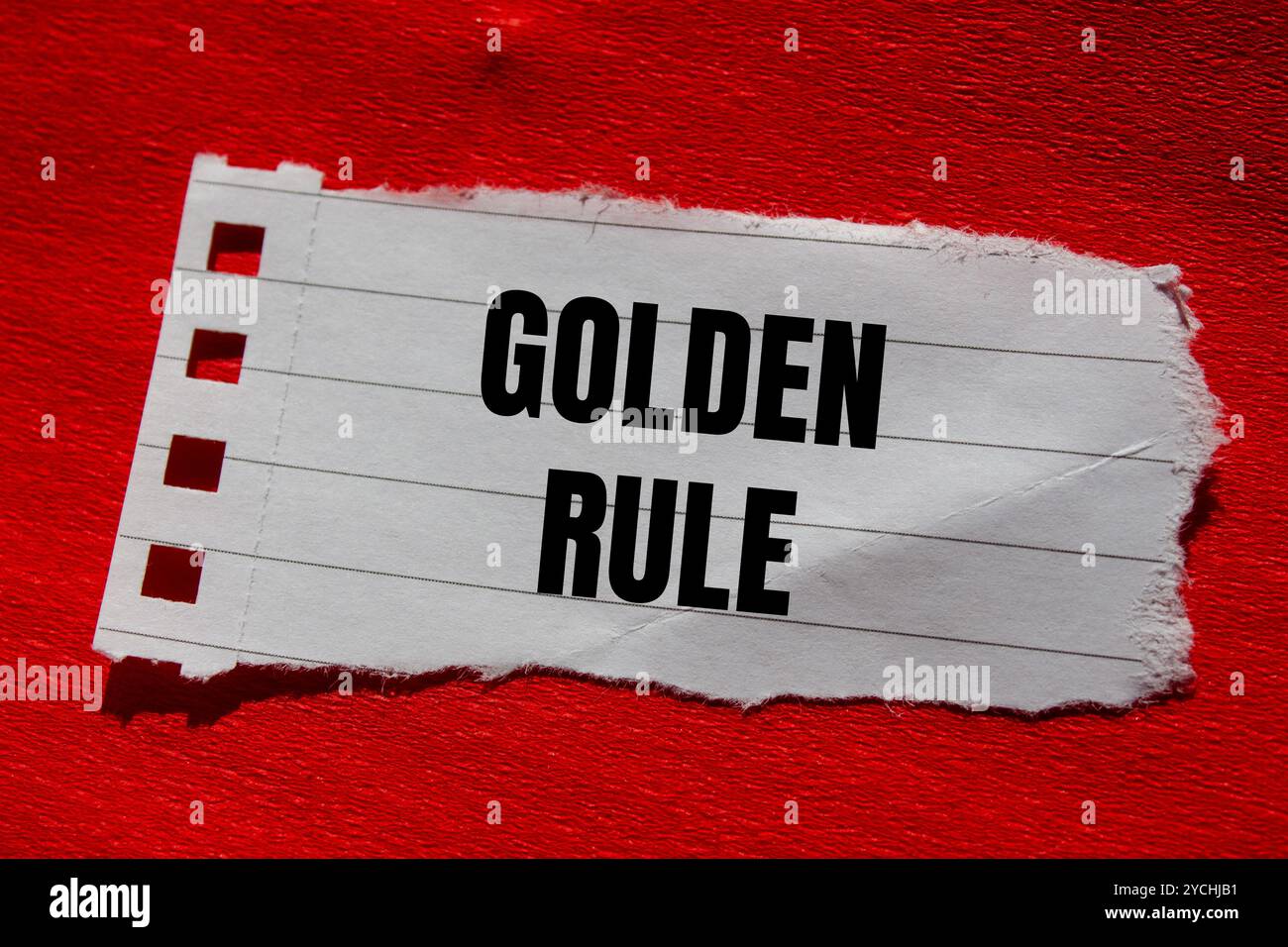 Goldene Regelnachricht auf gerissenem Papierstück mit rotem Hintergrund. Konzeptionelles goldenes Regelsymbol. Kopierbereich. Stockfoto