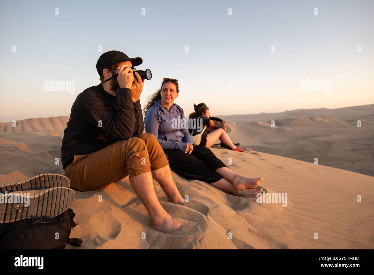 ICA, Peru – 3. August 2023: Junge Männer und Frauen starren und machen Fotos auf einer großen Düne in der Mitte der großen Wüstendünen, bekannt als Huacachi Stockfoto
