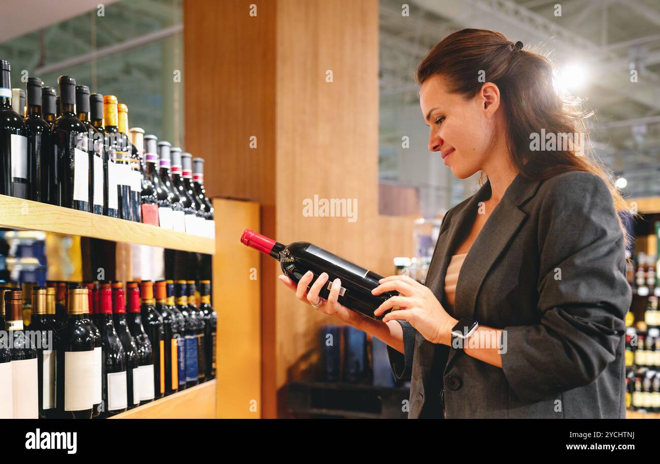 Erwachsene Brünette Frau in Anzug Jacke, die Wein im Weingeschäft auswählt Stockfoto