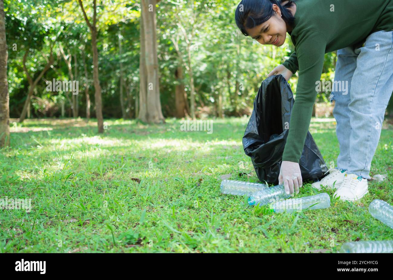 Frauen engagierter Freiwilliger nehmen an einer Umweltreinigungsaktion in einem Park Teil. Frau trägt Handschuhe und hält große schwarze Taschen. Frau Stockfoto